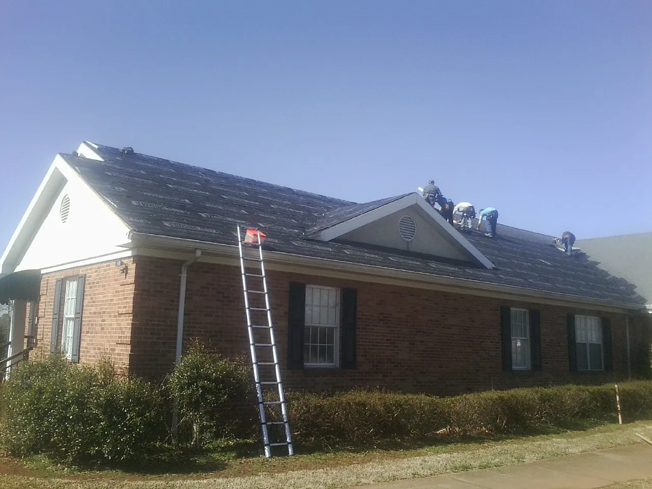 Crew tearing shingles off a brick ranch roof with a ladder set — Emergency Roof Repair work by our crew in Amherst
