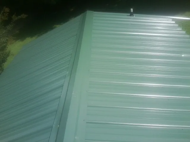 New green metal panels meeting at the ridge of a roof — Flat Roof Repair work by our crew in Amherst