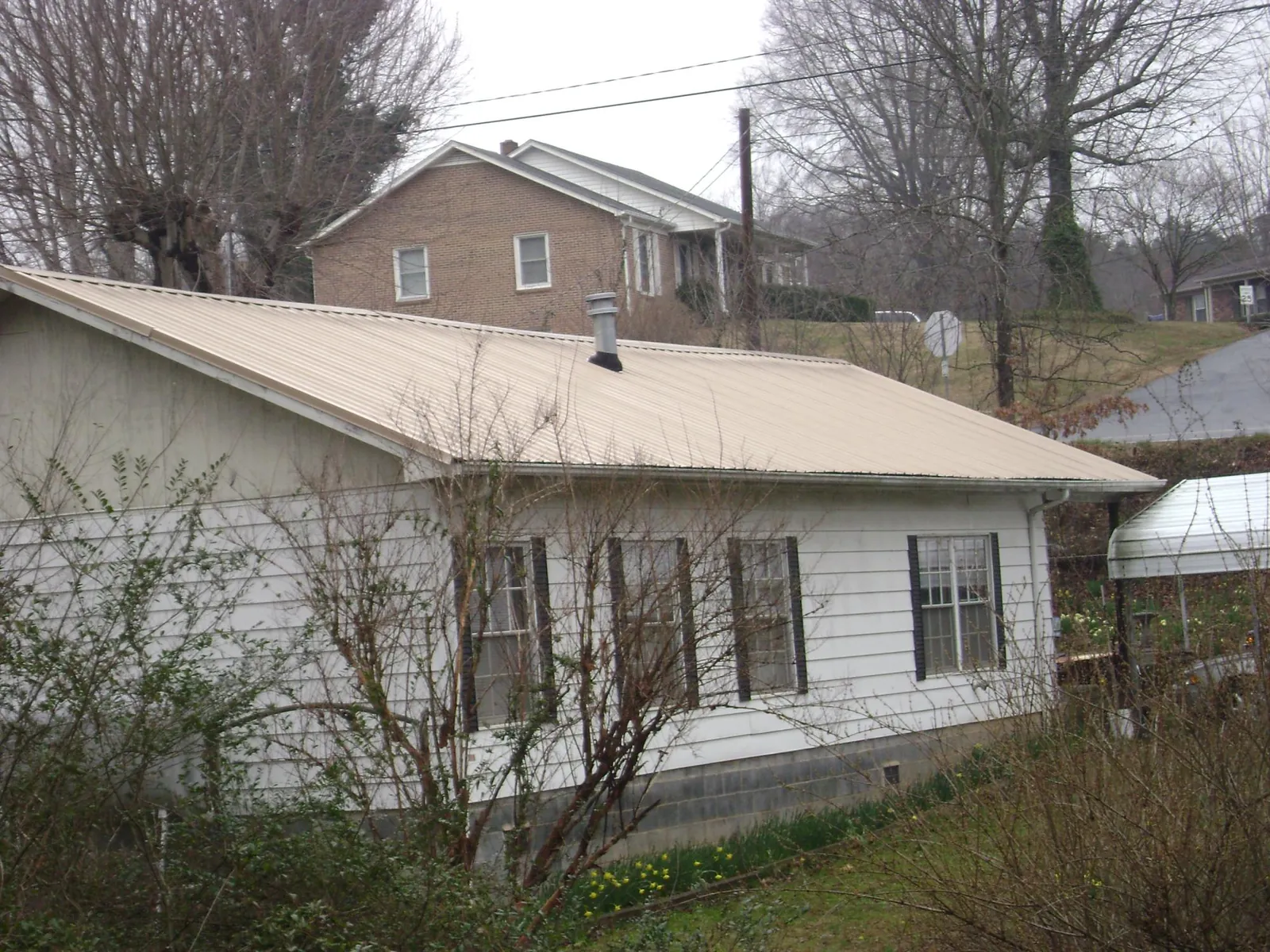 Tan metal roof on a white sided house set into a hillside — Commercial Roofing by Roofing Brothers in Amherst